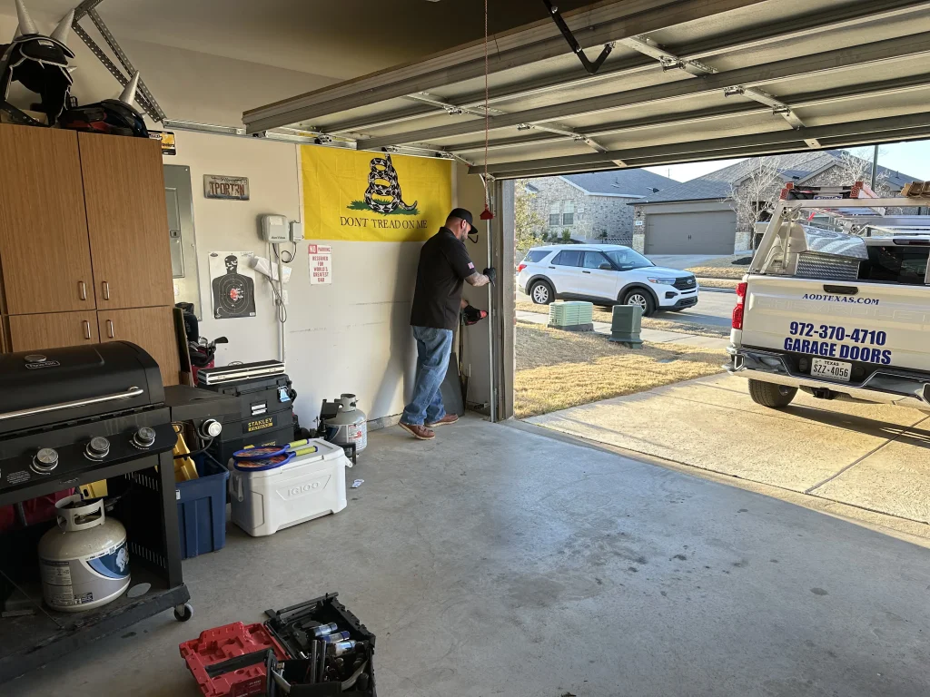 A service technician inspects the side tracking inside an open residential garage next to a company work truck, perfect for illustrating how to fix a garage door off-track.