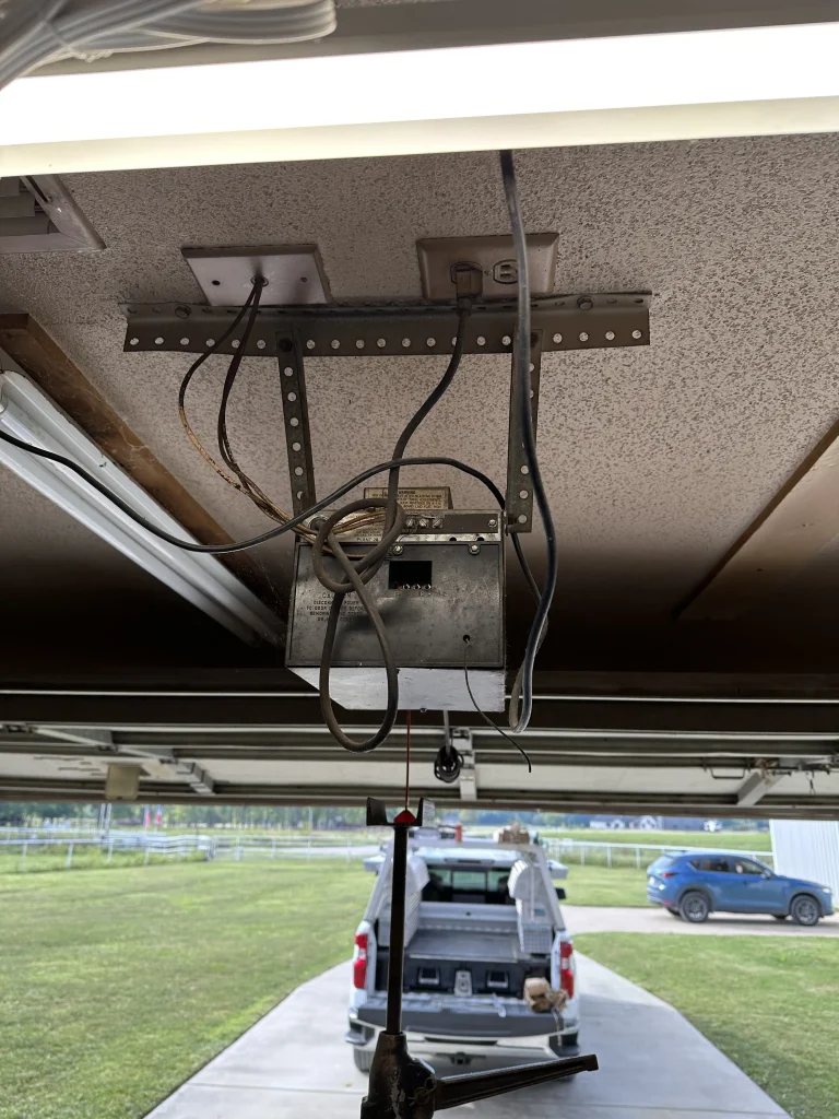 A close-up view of an older overhead garage door opener motor unit mounted to the ceiling, ideal for detailing the steps to change your garage door opener battery.