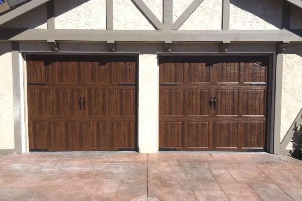 An exterior view of two side-by-side carriage-style wooden garage doors with prominent black handles and hardware, highlighting the aesthetic advantages of choosing modern wood garage doors.