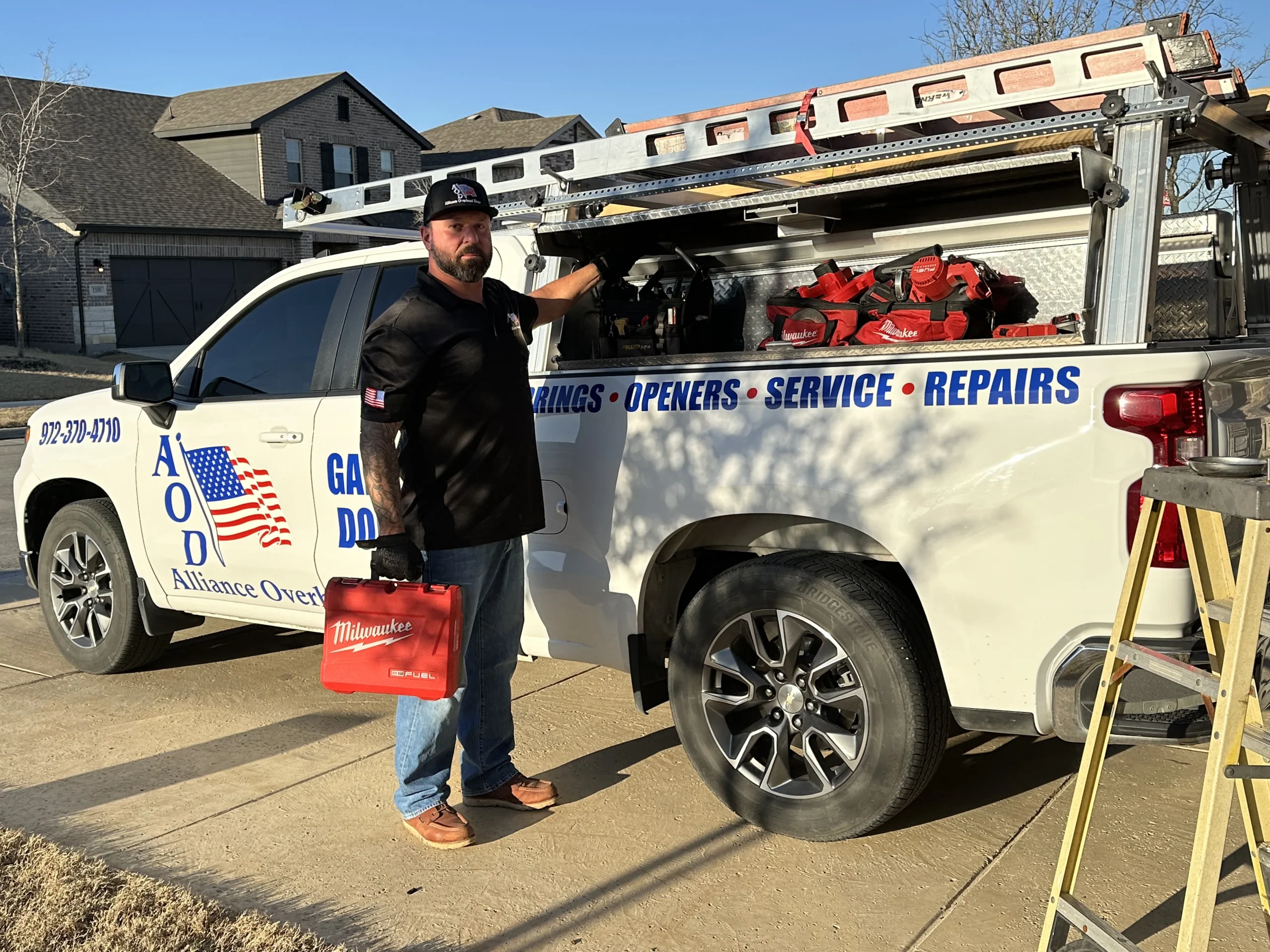 A service technician holding a tool case next to an Alliance Overhead Garage Doors service truck, highlighting the availability of professional garage door opener repair.