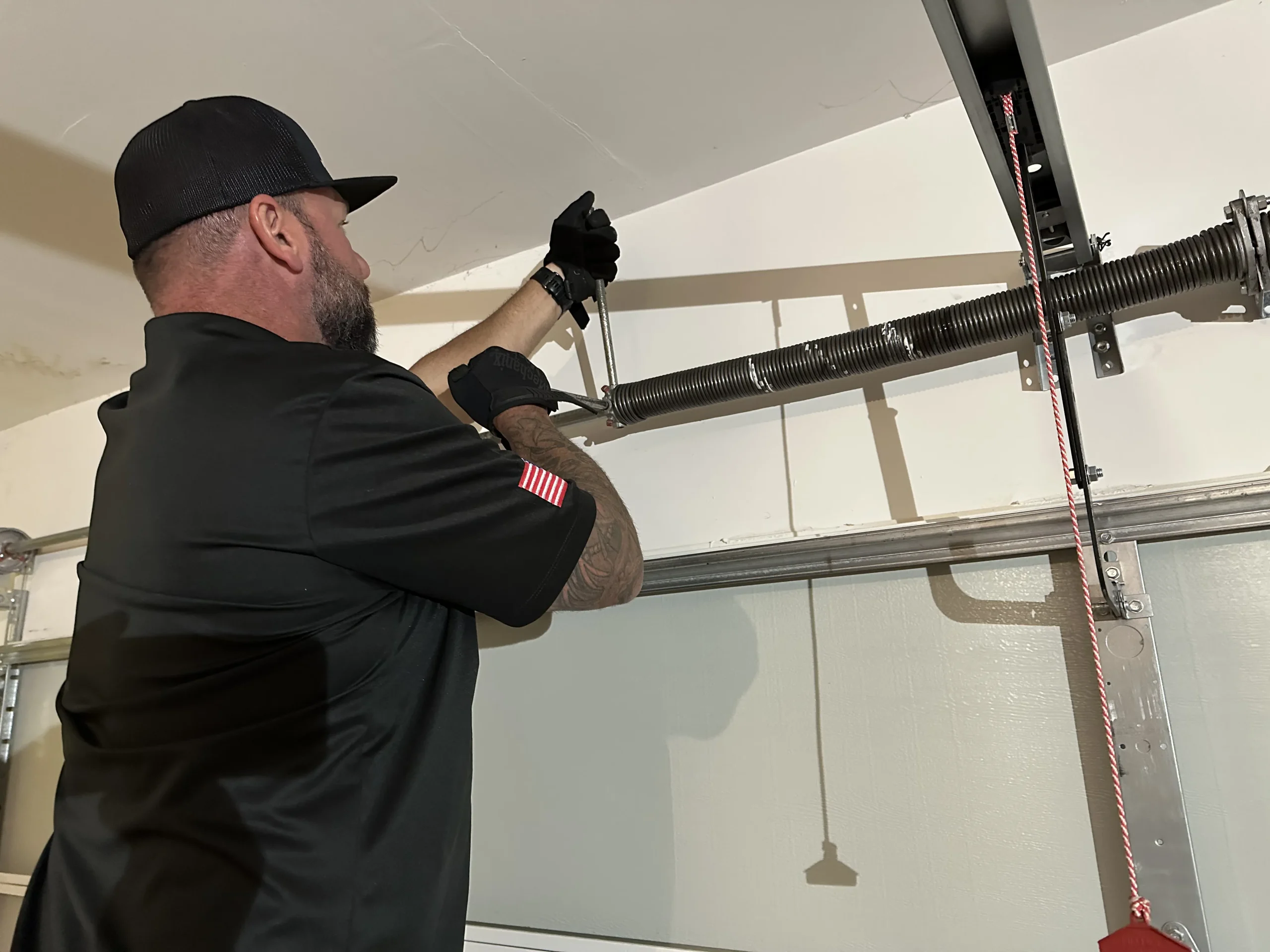 A service technician carefully uses winding bars to tension an overhead torsion spring, demonstrating essential safety tips to adjust a garage door system.