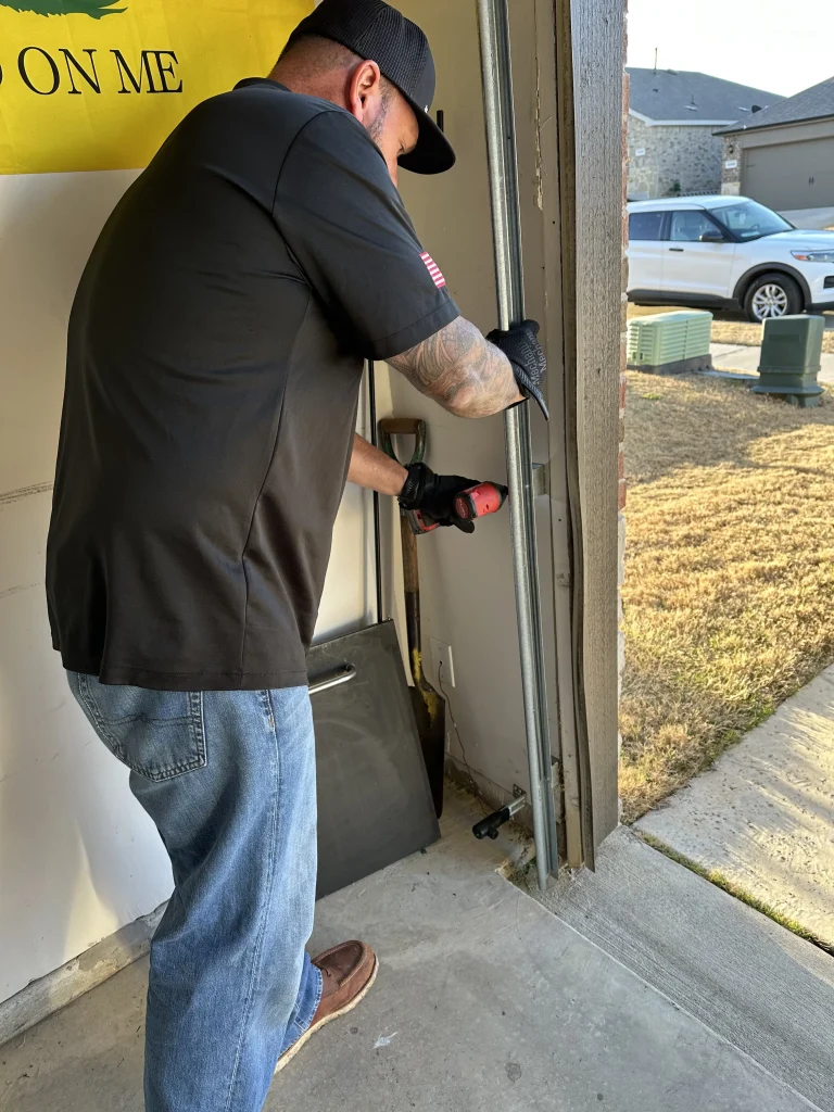 A service technician uses an impact driver to secure or adjust a vertical metal rail near the garage opening, demonstrating the alignment process for a bent garage door track.