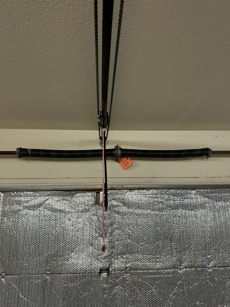 An interior overhead view of a dual torsion spring system mounted above a foil-insulated garage door, representing factors that influence a standard garage door spring lifespan.
