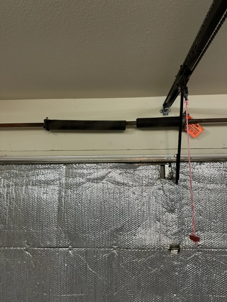 An interior overhead view of a broken torsion spring with a noticeable gap along the center shaft, offering a stark contrast to proper care tips on how to extend the life of a garage door spring.