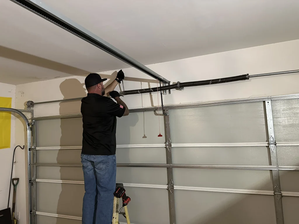 A technician on a ladder adjusting garage door springs above the door header to repair a Broken Torsion Spring.